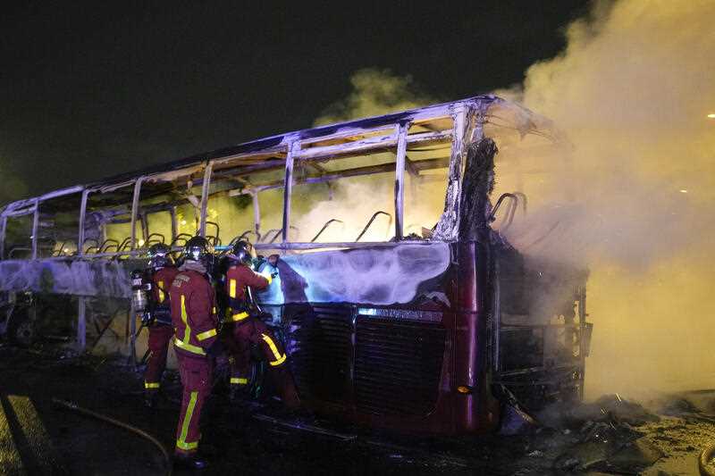 Firefighters use a water hose on a burnt bus in Nanterre, outside Paris, France, Saturday, July 1, 2023.