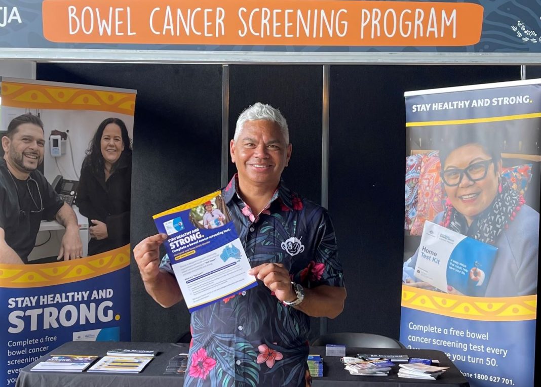 Smiling Aboriginal Australian man John Paul Janke holding a free bowel cancer screening test kit