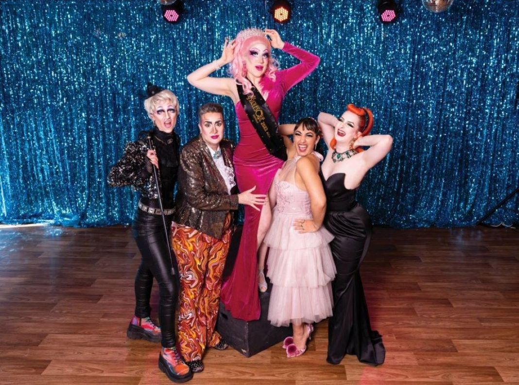 2 drag kings and 3 burlesque performers pose in front of blue sequin curtain