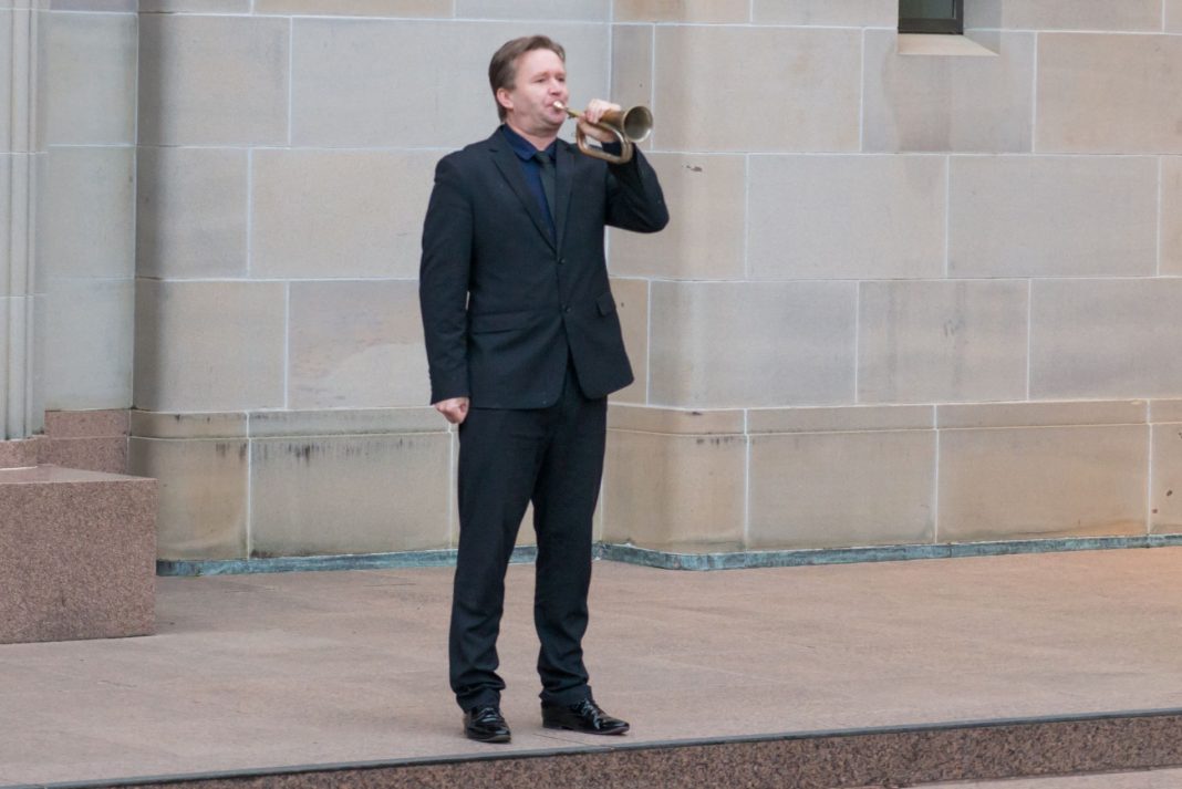 man in suit playing The Last Post on the bugle at the Australian War Memorial