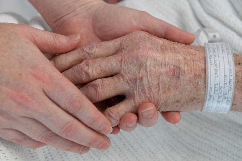 A nurse holds the hand of an elderly patient wearing a hospital identification band