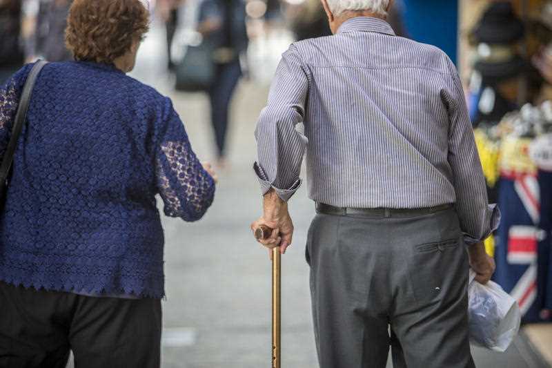 rear view of an elderly couple seen walking along a footpath outside shops