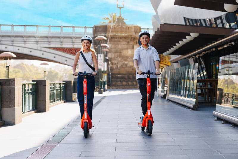 a man and a woman riding Neuron e-scooters in Melbourne