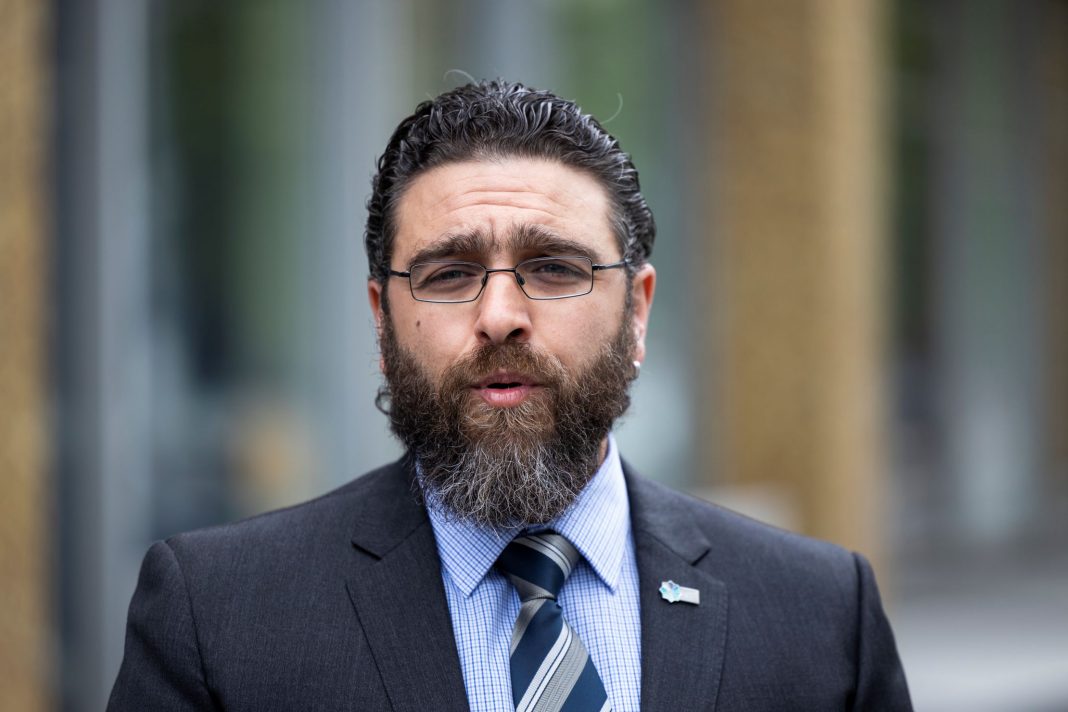 Bearded middle aged man wearing spectacles, a dark navy suit and blue striped tie, Alex Caruana from the Australian Federal Police Association is seen speaking to the media