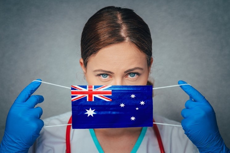 female medical professional holding face mask depicting Australian flag across their nose and mouth