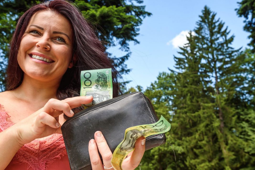 Smiling woman extracting Australian $100 notes from a black leather wallet