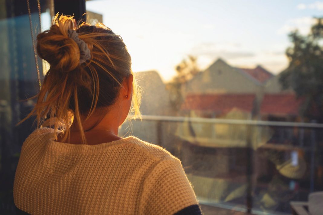 young woman looking out the window at setting sun