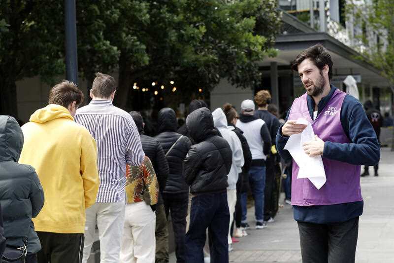 An AEC staff member is seen with voters waiting in long queues outside the voting centre at Docklands Library in Melbourne, Saturday, October 14, 2023