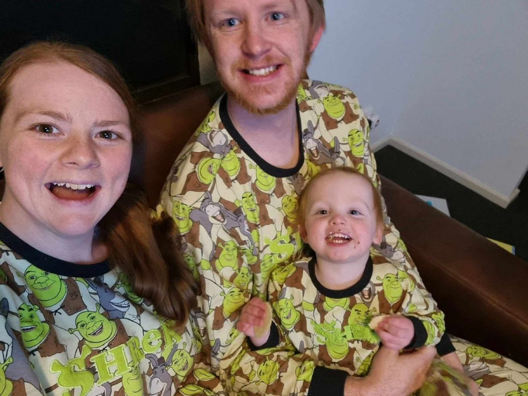 smiling mum and dad with 2-year-old boy all dressed in Shrek pyjamas