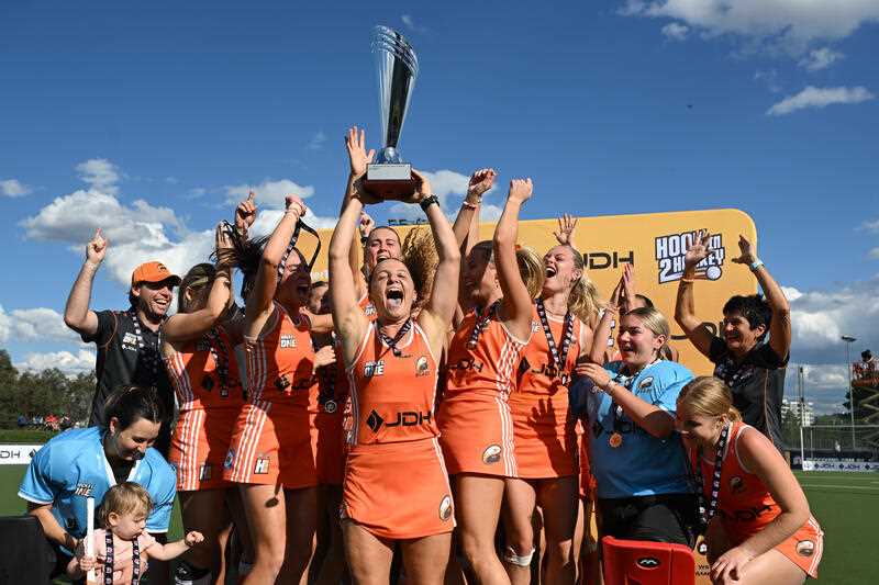 Players of the Brisbane Blaze in orange kit celebrate with the winner’s trophy after the Womens Final of the Hockey One League 2023 Finals series between the Brisbane Blaze and the Canberra Chill at the National Hockey Centre in Canberra
