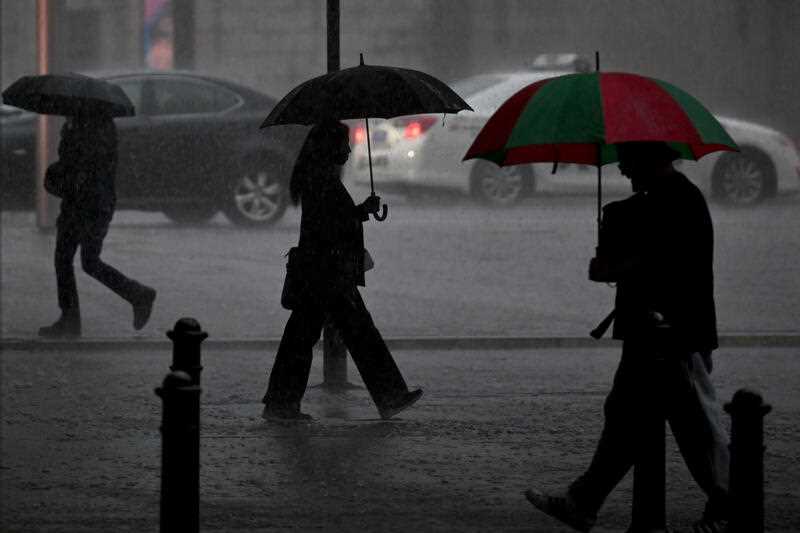 3 pedestrians are seen walking under umbrellas during heavy rain in Sydney city
