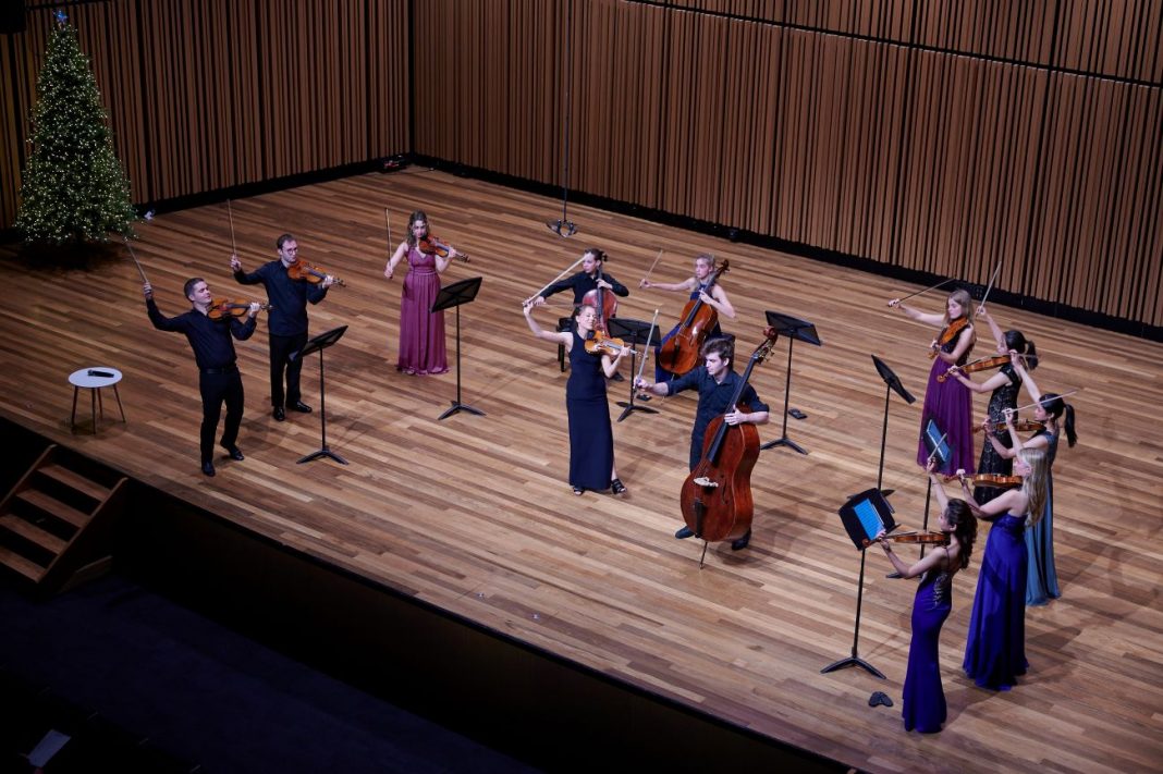 12 young musicians on stage playing various string instruments