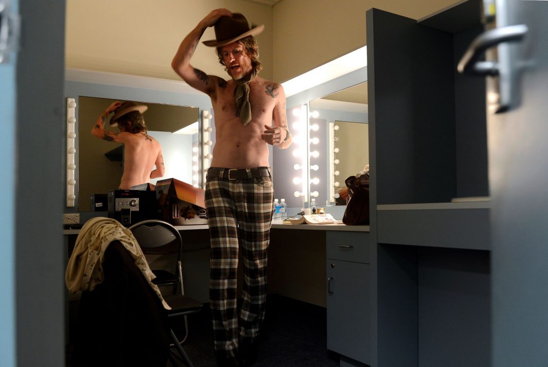 shirtless male rock singer wearing check pants and a Akubra in a dressing room