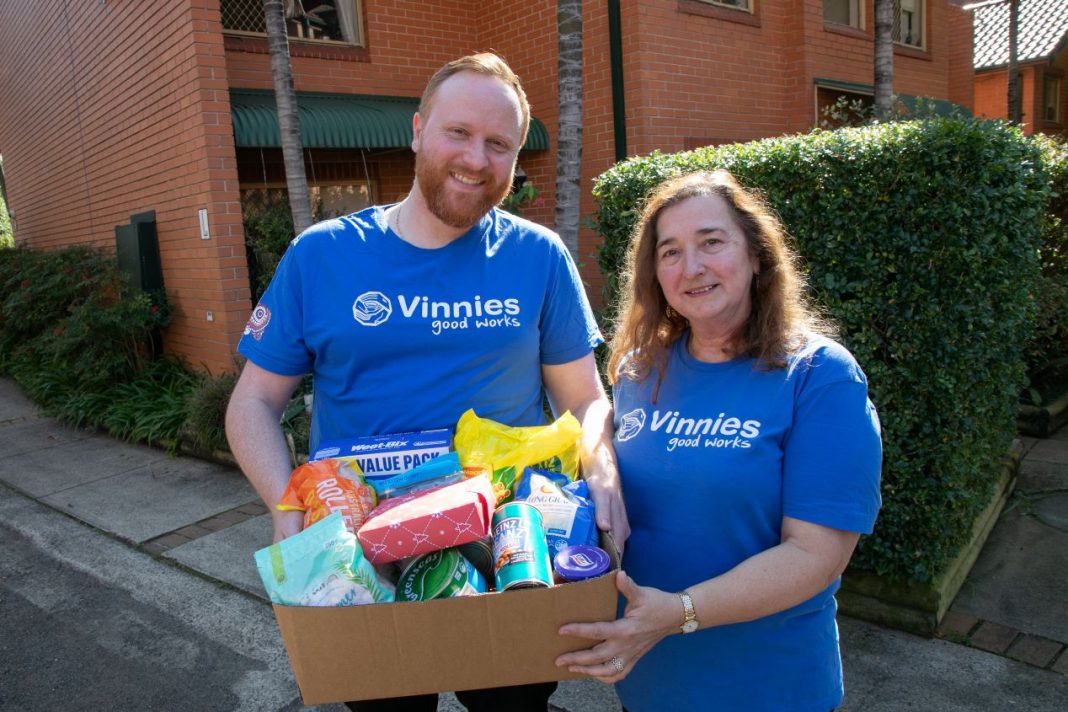man and woman in blue Vinnies volunteer T-shirts delivering a box of groceries