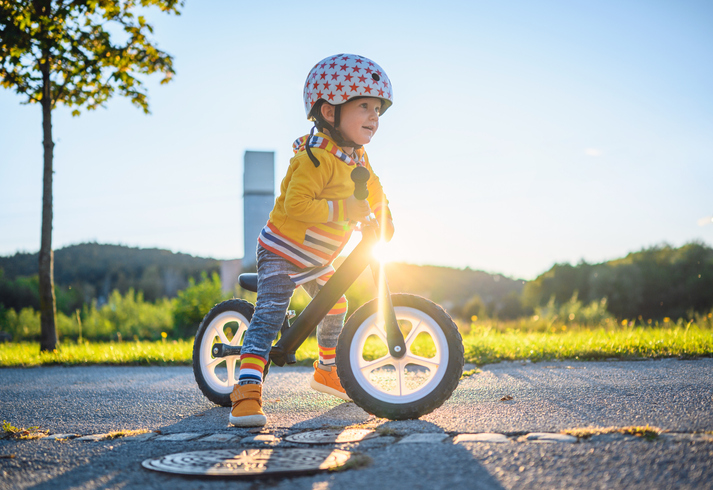 Preschool child wearing a bike helmet and riding a balance bike outdoors on a sunny day