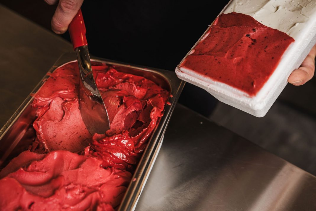 hands seen scooping raspberry gelato into a container
