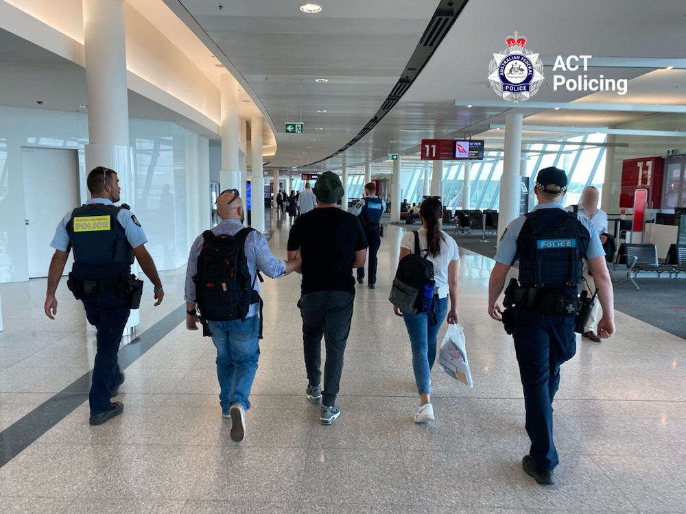 A 29yo man is escorted by police and protective service officers through Canberra Airport. Photo supplied