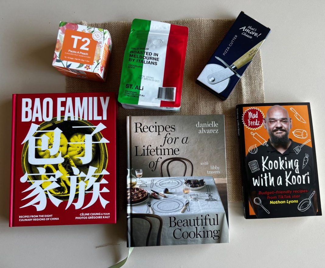 3 cookbooks, bag of coffee beans, packet of tea and a pizza cutter displayed on table