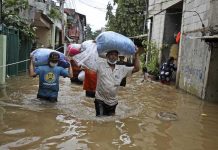 Indonesian men carry their belongings as they wade through the water at a flooded neighborhood