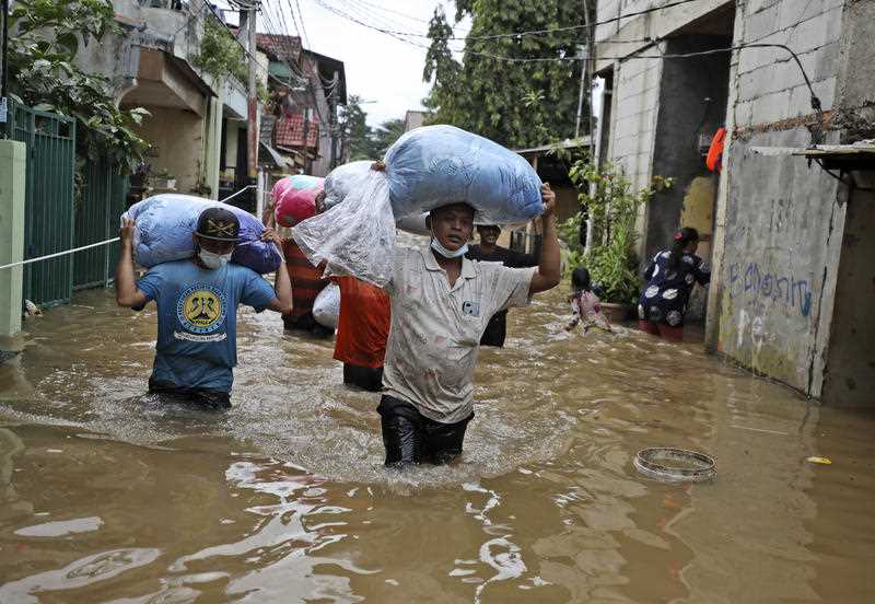 Indonesian men carry their belongings as they wade through the water at a flooded neighborhood