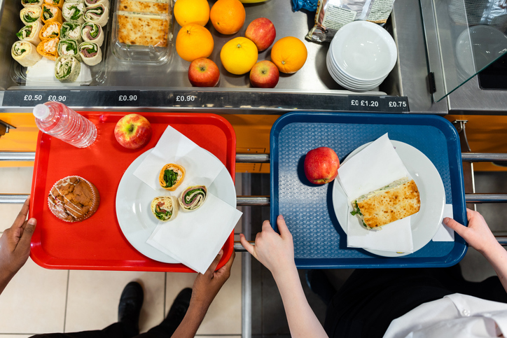 An aerial view of two high school students with snacks for lunch out their trains in the school cafeteria in the school they go to in the North East of England. On display in the chiller fridge is lots of fruit and healthy options for lunch.